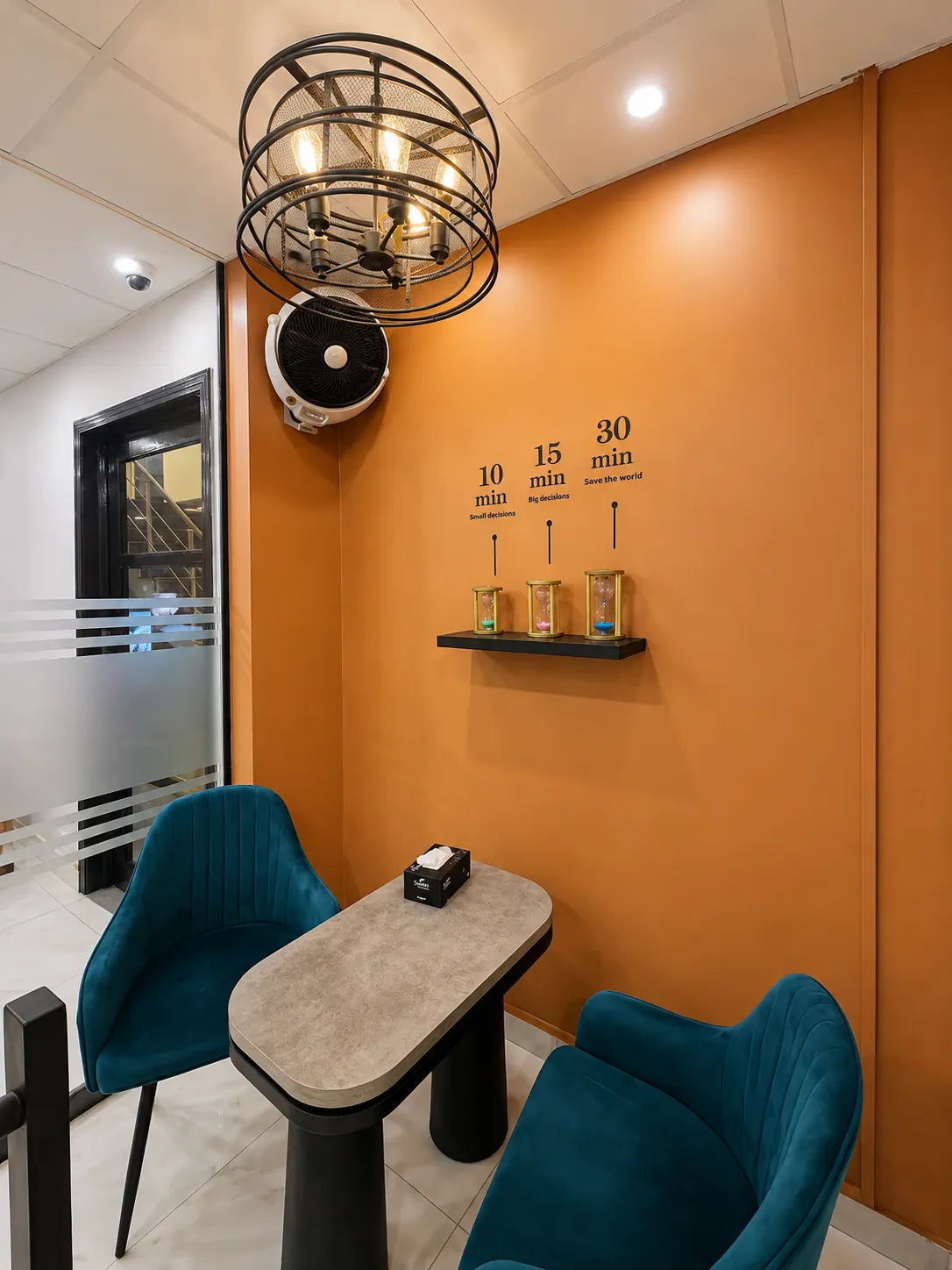 A huddle room at WorkBench: two teal chairs facing a small table against a terracotta wall, with hourglasses on a shelf