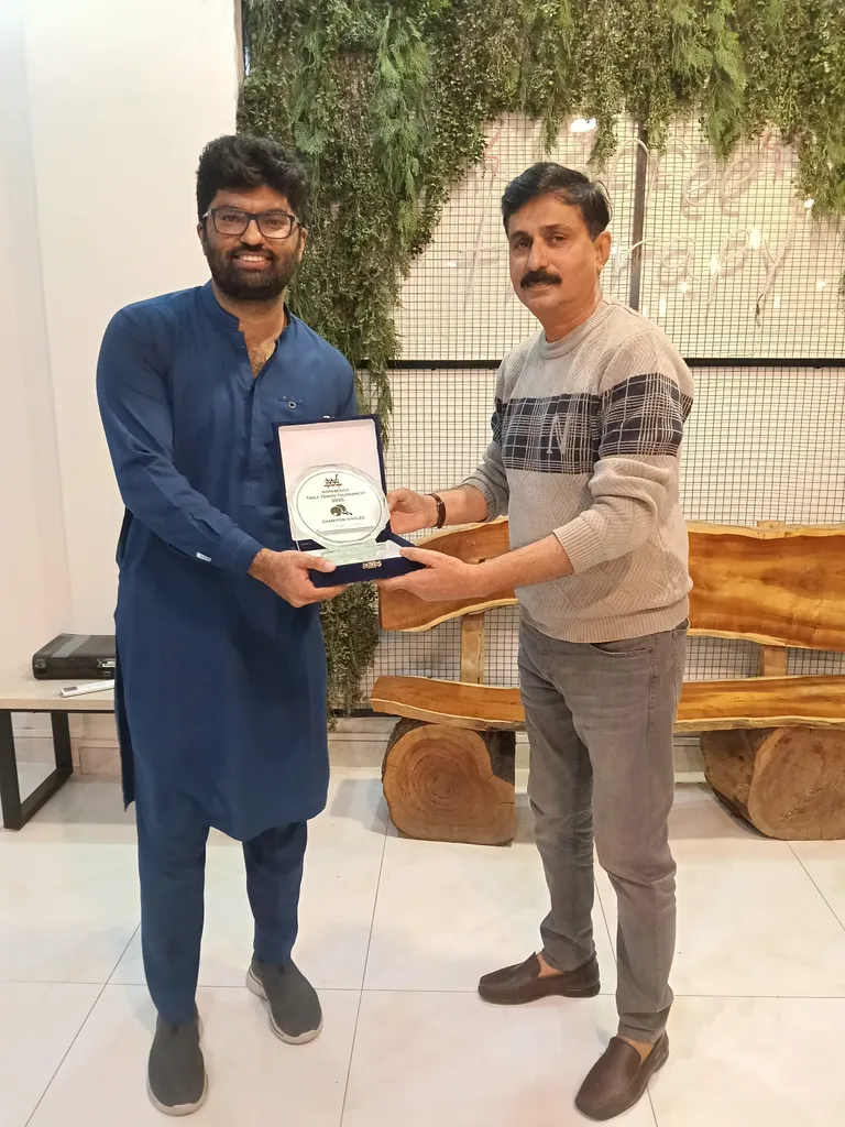 Two men presenting a tournament plaque in front of the greenery wall