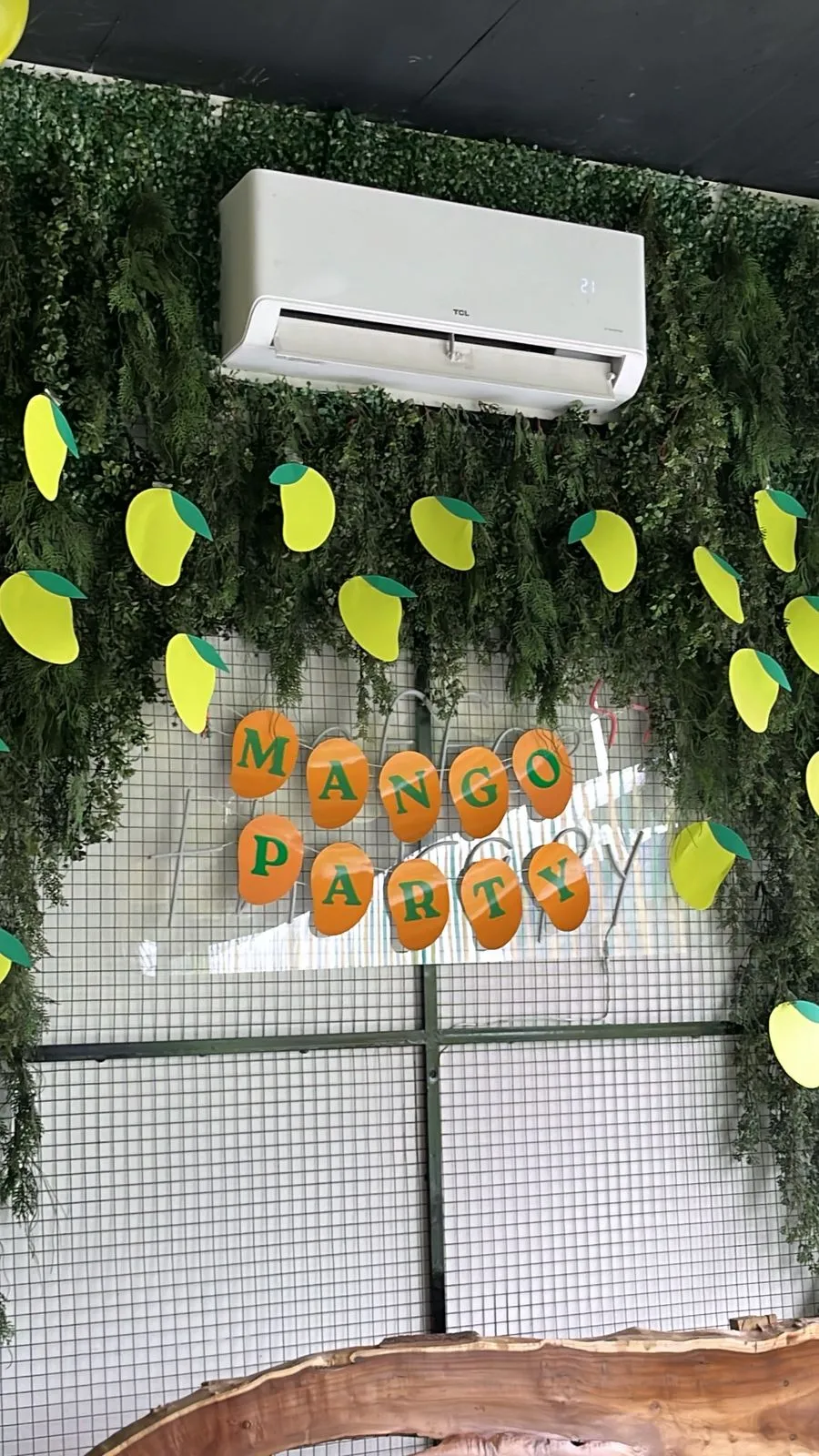 A Mango Party sign spelled out in orange paper mangoes on a green plant wall at WorkBench, with yellow and green paper mangoes pinned all around it.