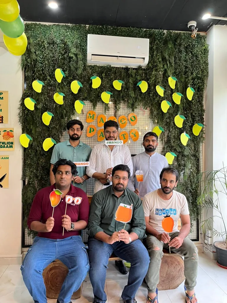 Six members posing with mango props in front of the Mango Party wall