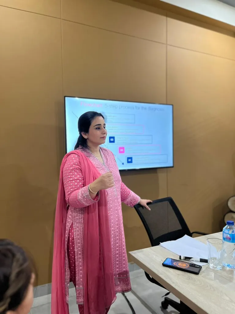 A speaker in pink presenting slides on a screen in a meeting room