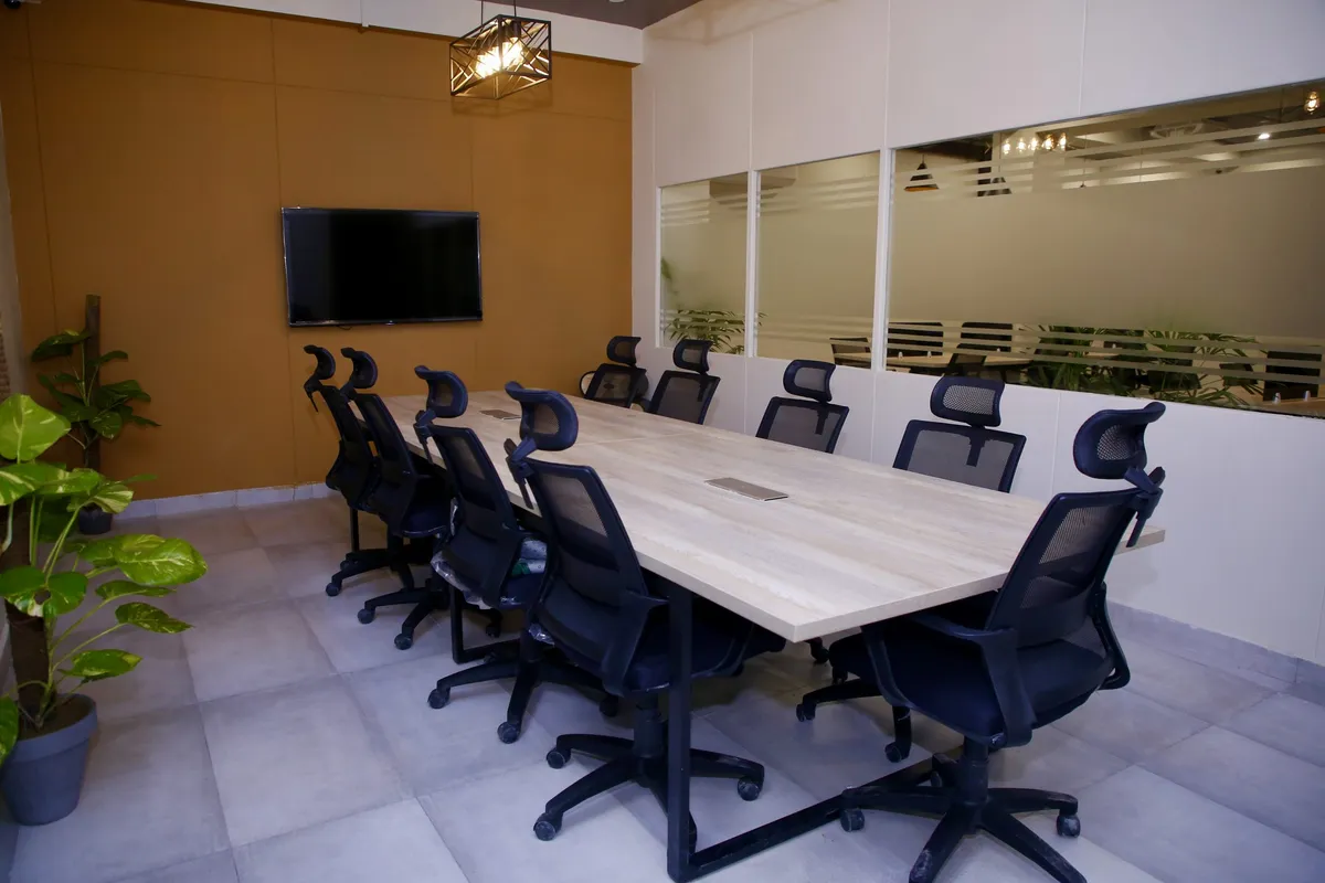 The conference room at WorkBench, a long white table with ten black mesh chairs, a wall mounted screen on the terracotta wall and a caged pendant light overhead.
