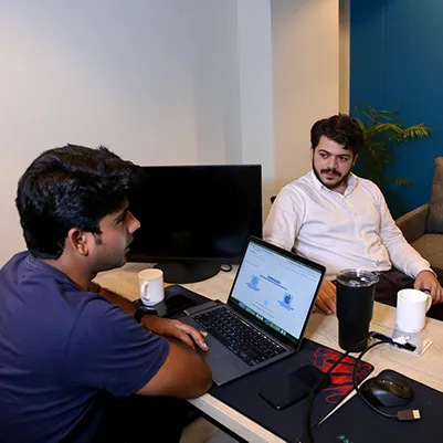 Two colleagues working at desks inside a private office with a monitor and a plant