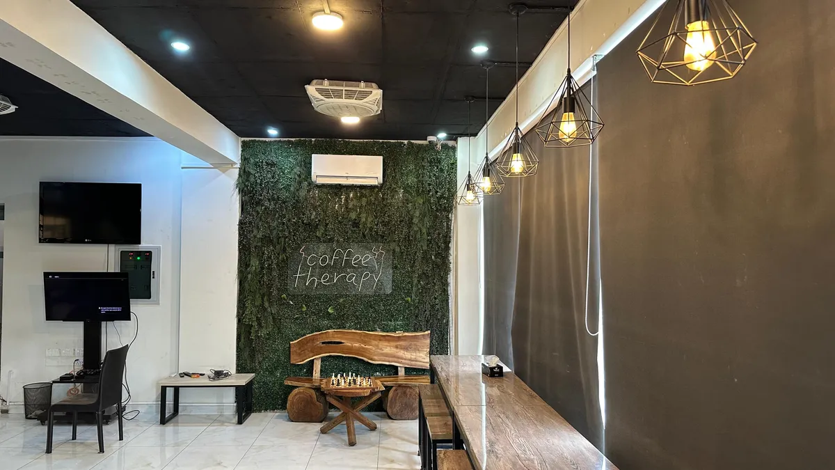 The coffee therapy room at WorkBench, with a moss wall, a live edge wooden bench, a chess set on a round table and cage pendant lights.