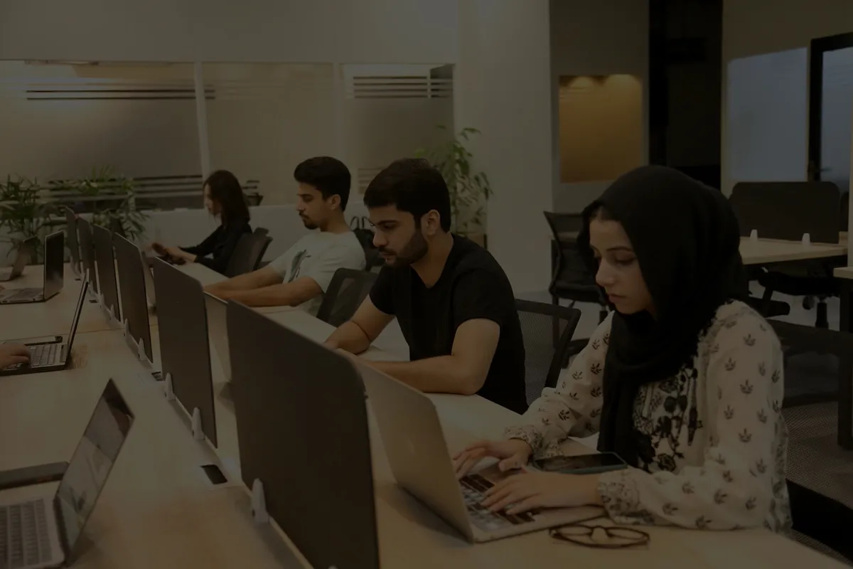 Four members working side by side at a long desk at WorkBench, laptops open and privacy dividers between them.