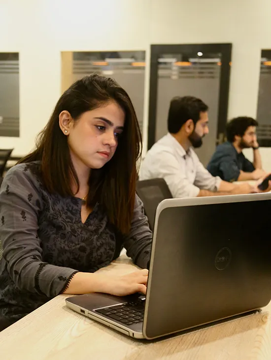 A member at WorkBench working on a laptop at a long desk, with two colleagues at the same run of desks behind her.